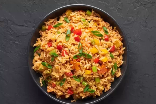 Veg Schezwan Fried Rice in black bowl at dark slate background. Vegetarian Szechuan Rice is indo-chinese cuisine dish with bell peppers, green beans, carrot. Top view